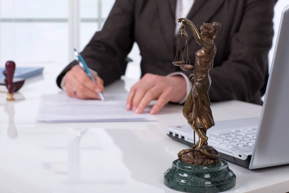 Image is of an attorney reviewing and signing legal documents beside a Lady Justice statue, concept of a criminal defense lawyer preparing a strategic defense for criminal charges.